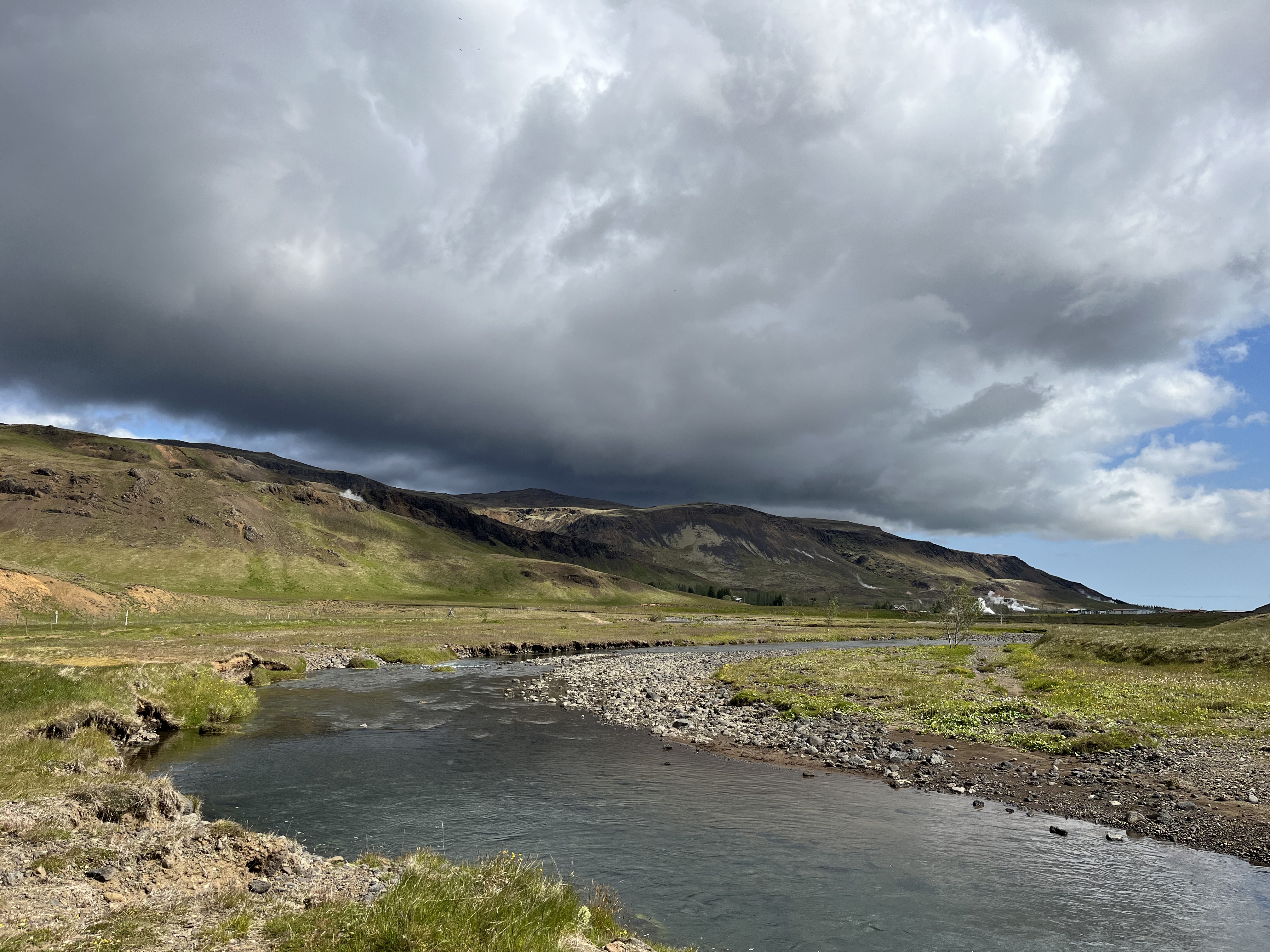 Plaine islandaise avec collines, rivière et nuages sombres